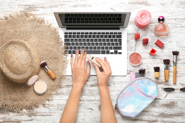 Mãos de blogueira de beleza feminina com laptop, cosméticos de maquiagem e acessórios em fundo de madeira
 - Foto, Imagem