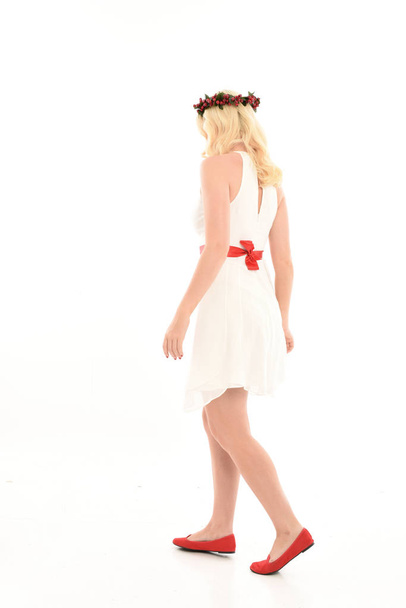 白いドレスと花冠を着たブロンドの女の子の完全な長さの肖像画。立ったポーズ、赤いプレゼントを持ち、白いスタジオの背景に隔離. - 写真・画像