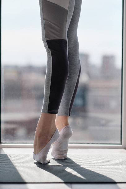 Close-up of female legs in sportswear and socks. Training of dance moves and stretching on the balcony against the window. - Foto, Bild