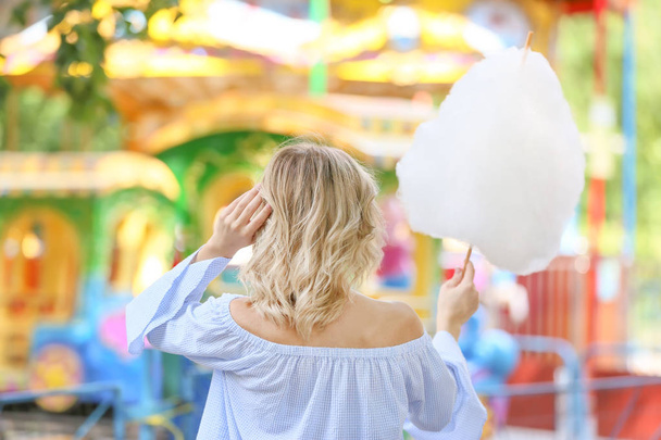 Mujer con dulce algodón de azúcar en el parque de atracciones, vista trasera
 - Foto, imagen