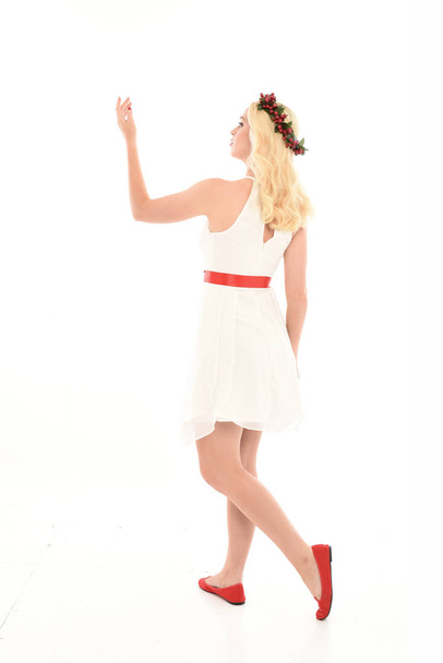 täyspitkä muotokuva blondi tyttö yllään valkoinen mekko ja kukka kruunu. Seisova asento, tilalla punainen läsnä, eristetty valkoinen studio tausta
. - Valokuva, kuva