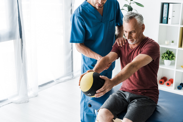 обрезанный вид врача, стоящего рядом с зрелым человеком, упражняющимся с мячом
  - Фото, изображение