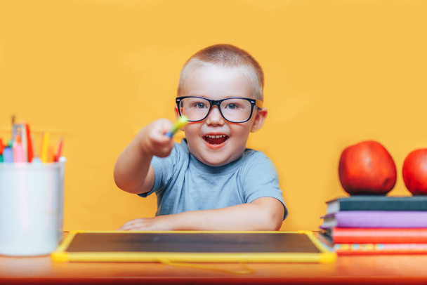 Маленький мальчик рисует и делает домашние работы на своем столе, имея идею, концепцию вдохновения. назад в школу на желтом фоне
 - Фото, изображение