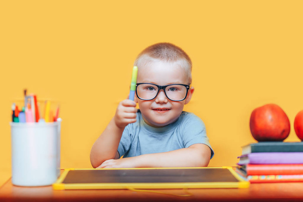 Niño pequeño pintando y haciendo deberes en su escritorio teniendo una idea, concepto de inspiración. volver a la escuela sobre fondo amarillo
 - Foto, imagen