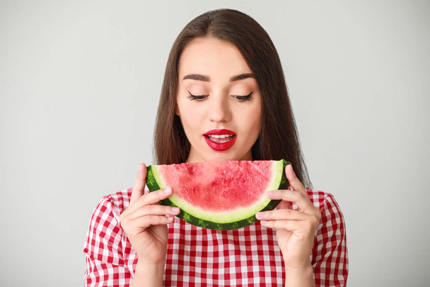 Krásná mladá žena s plátkem čerstvého melounu na světlém pozadí - Fotografie, Obrázek