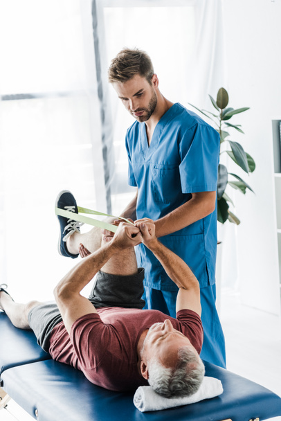 knappe arts Holding been van volwassen patiënt trainen met elastiek  - Foto, afbeelding