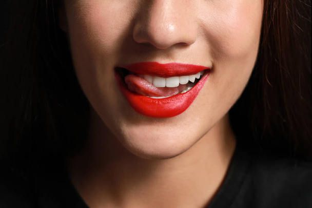 Kaunis nuori nainen, jolla on kirkas huulipuna tummalla taustalla, lähikuva
 - Valokuva, kuva