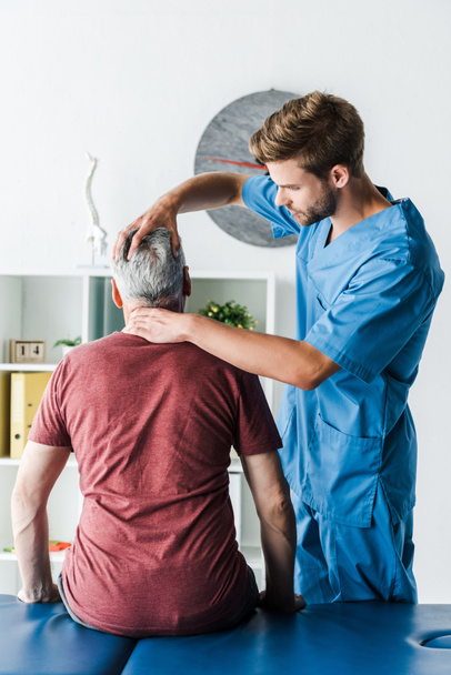 красивый бородатый врач трогает голову пациента среднего возраста в клинике
 - Фото, изображение