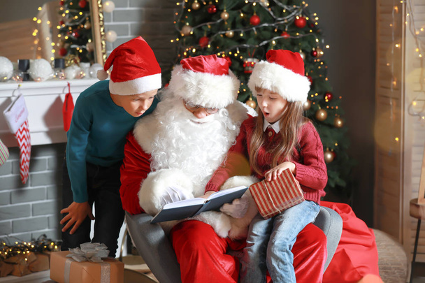 Le Père Noël et les petits enfants lisent le livre dans la chambre décorée pour Noël
 - Photo, image