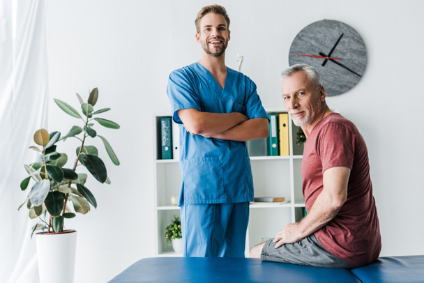 handsome doctor standing with crossed arms near happy patient  - Foto, immagini