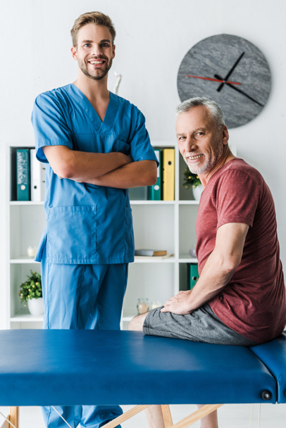 cheerful doctor standing with crossed arms near happy patient  - Valokuva, kuva