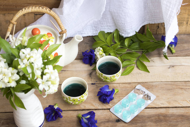 трав'яні здорові напої синя вода екстракт метелика горохові квіти і розквіт кашлю таблетки для догляду за здоров'ям з квітковими композиціями плоский стиль на фоні дерев'яного
 - Фото, зображення