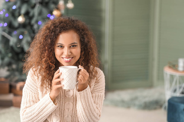 Young African-American woman drinking hot chocolate at home on Christmas eve - Valokuva, kuva