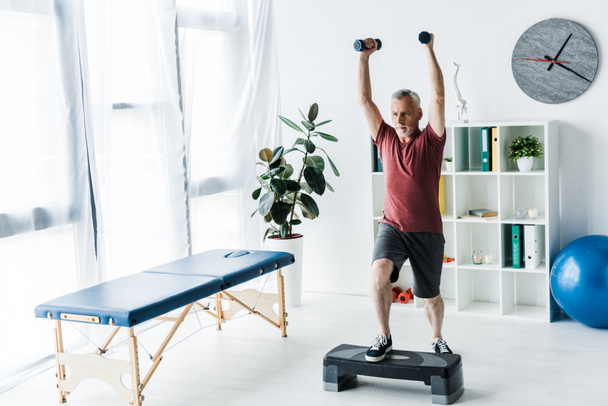bearded mature man exercising with dumbbells in clinic   - Foto, Imagen