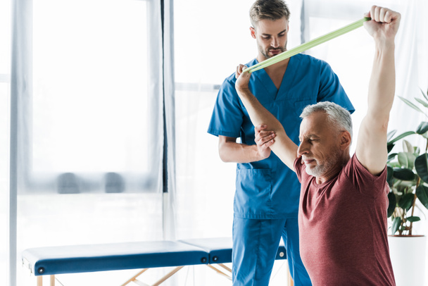 doctor standing near middle aged man exercising with resistance band  - Photo, Image