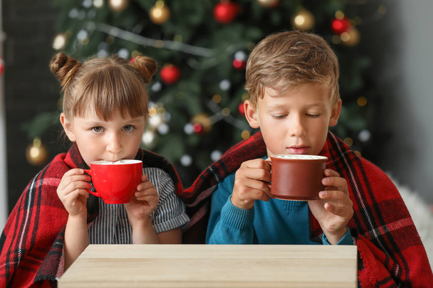 Χαριτωμένα μικρά παιδιά που πίνουν ζεστή σοκολάτα στο σπίτι την παραμονή των Χριστουγέννων - Φωτογραφία, εικόνα