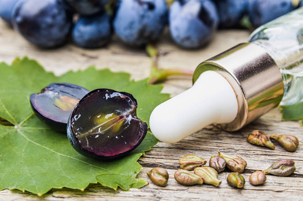 Olio di semi d'uva in una bottiglia di vetro vicino uva blu e foglie verdi su vecchie tavole di legno. Spa, concetto di prodotti ecologici
. - Foto, immagini