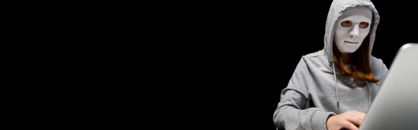 панорамный снимок анонимного интернет-тролля в маске с помощью ноутбука, изолированного на черном
 - Фото, изображение