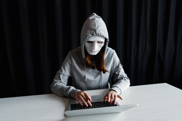 anonymous internet troll in mask typing on laptop keyboard on black - Photo, Image