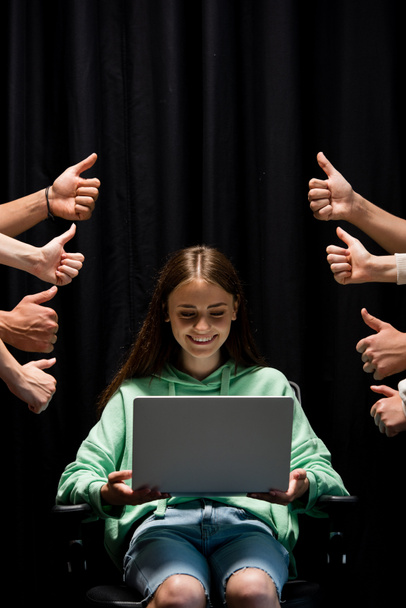 vue partielle de personnes montrant pouces levés et souriant fille tenant ordinateur portable sur noir
 - Photo, image