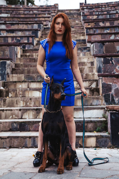 schöne Besitzerin mit ihrem Hund schwarzem Dobermann im Freien spazieren gehen - Foto, Bild