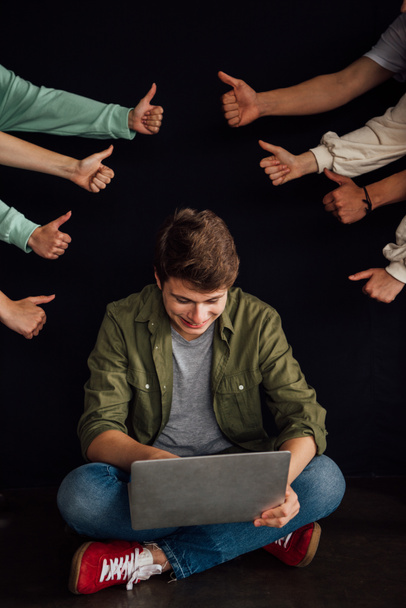 частичный вид подростков, показывающих большие пальцы вверх и улыбающийся мальчик с помощью ноутбука изолированы на черном
 - Фото, изображение