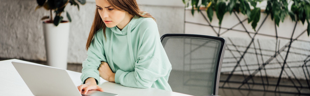 панорамний знімок засмученої дівчини, що сидить за столом і використовує ноутбук вдома
 - Фото, зображення