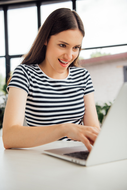 smiling girl in striped t-shirt using laptop at home - Photo, Image