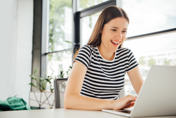 smiling girl in striped t-shirt using laptop at home - Fotó, kép