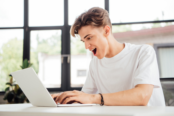 excited teen boy in white t-shirt using laptop at home - Photo, Image