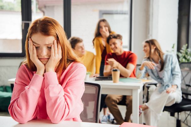 sad girl sitting in front of laughing classmates - Photo, Image