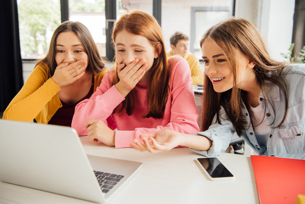 three excited smiling girls looking at laptop screen in school - Photo, Image
