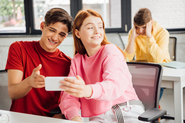 two friends smiling while using smartphone in school - Photo, Image