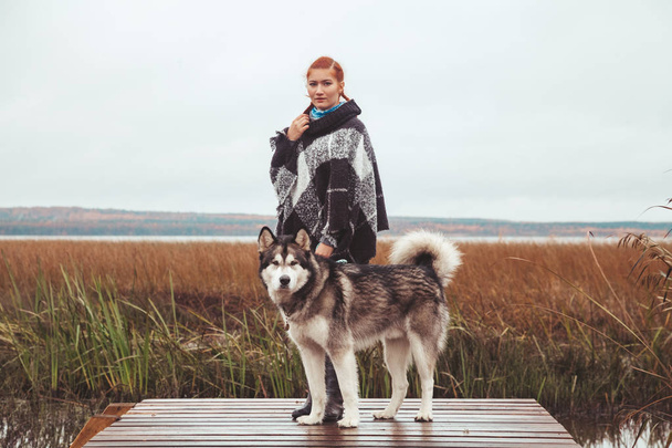 redhaired caucasian woman owner with her malamute grey big dog near the lake - Photo, Image