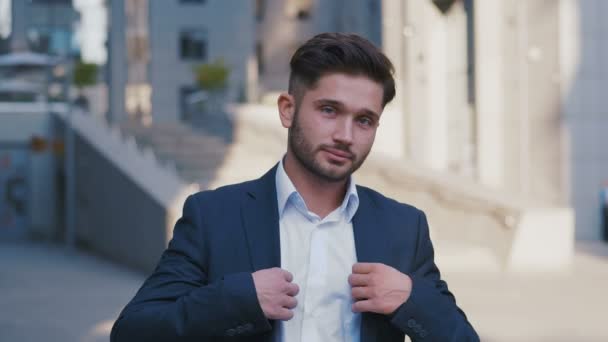 Πορτρέτο του επιτυχημένου νεαρού επιχειρηματία που στέκεται στην πόλη κοντά στο Επιχειρηματικό κέντρο απολαμβάνοντας τον επαγγελματικό αστικό τρόπο ζωής. Όμορφος άνδρας εργαζόμενος κοιτάζοντας την κάμερα. - Πλάνα, βίντεο