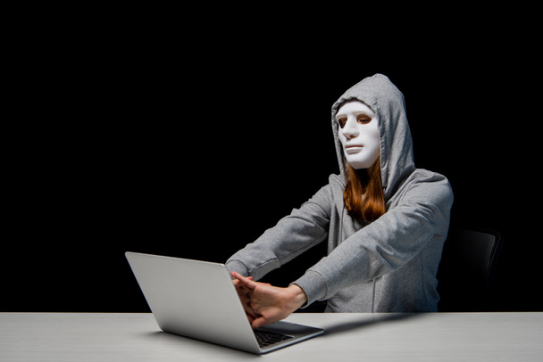 névtelen lány maszk és kapucnis pulcsit mellett ülve laptop és stretching kezet során cyberbullying elszigetelt fekete - Fotó, kép