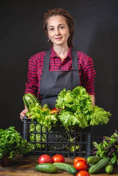 女性農家さんが新鮮な野菜とグリーンサラダ付きの箱を持っています。農場で栽培された有機農産物. - 写真・画像