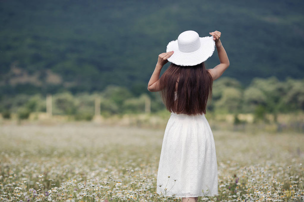 Красива дівчина на відкритому повітрі з букетом квітів в полі білих ромашок, насолоджується природою. Красива модель з довгим волоссям у білій сукні, розважається на літньому полі з квітучими квітами, сонячне світло. Молода щаслива жінка на весняному лузі, в сільській місцевості
 - Фото, зображення