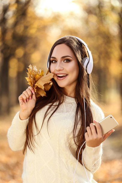 Beautiful woman holding maple leafs and smartphone in autumn par - Zdjęcie, obraz