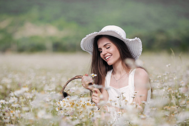 Beautiful girl outdoors with a bouquet of flowers in a field of white daisies,enjoying nature. Beautiful Model with long hair in white dress having fun on summer Field with blooming flowers,Sun Light. Young Happy Woman on spring meadow, countryside - Photo, Image