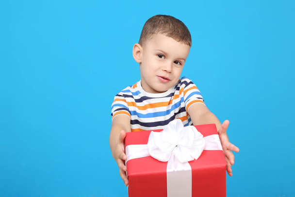 Cute little boy with gift box on blue background - Фото, изображение
