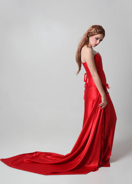 retrato de longitud completa de una niña con un vestido largo de seda roja, pose de pie sobre un fondo gris estudio
. - Foto, imagen