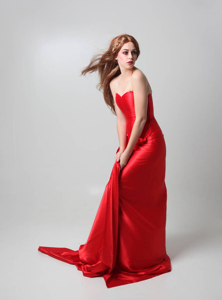 Pełna długość Portret dziewczyny ubrana w długą czerwoną suknię jedwabną, stojący stwarzają na szarym tle Studio. - Zdjęcie, obraz