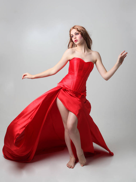retrato de longitud completa de una niña con un vestido largo de seda roja, pose de pie sobre un fondo gris estudio
. - Foto, Imagen