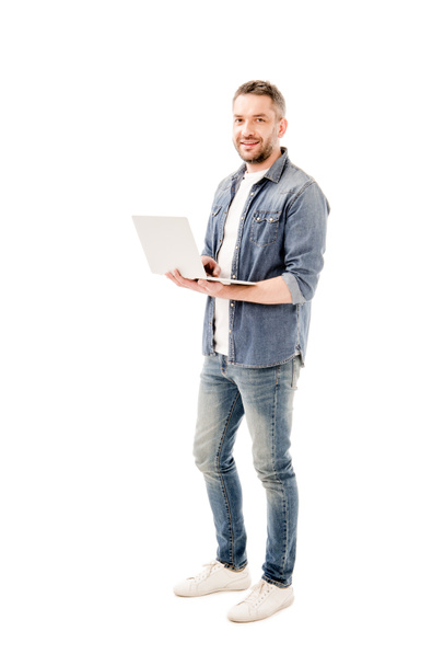 piena lunghezza vista di uomo sorridente in camicia di jeans che tiene il computer portatile isolato su bianco
 - Foto, immagini