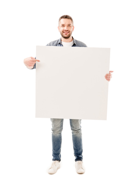 Plná délka pohled na usmívajícího se vousatého muže, který drží prázdnou placardu izolovaný na bílém - Fotografie, Obrázek