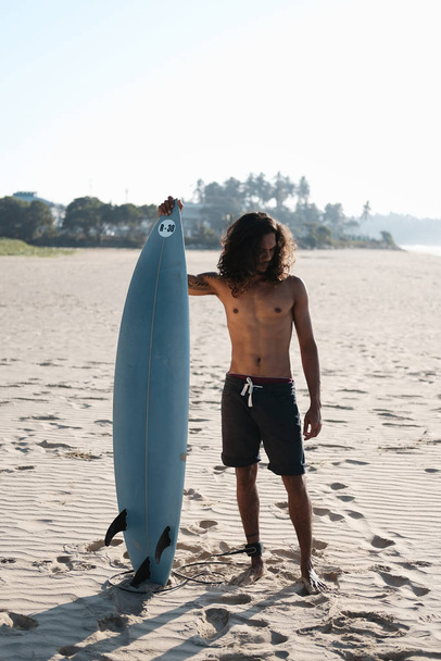 Man Surfer Sitting at Surfboard on Sand Beach - Foto, afbeelding