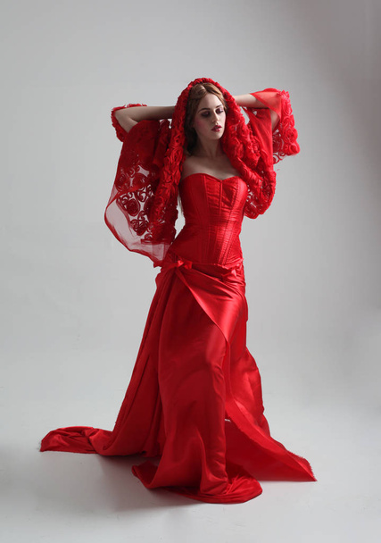 Ganzkörperporträt eines Mädchens in einem langen roten Seidenkleid, das vor grauem Studiohintergrund posiert. - Foto, Bild