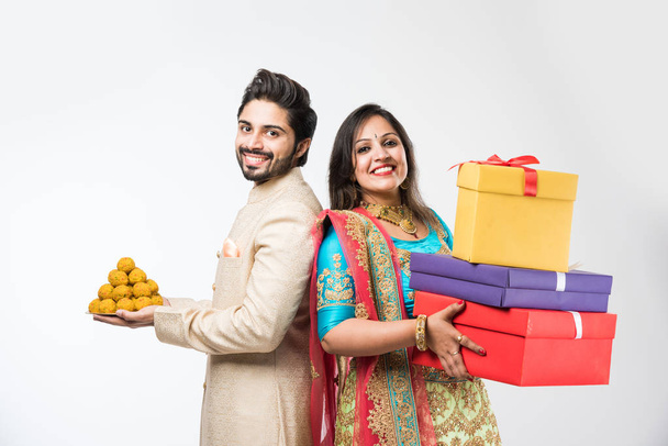 Laddu ve diwali / festival üzerinde hediye kutuları ile Hint çift, beyaz arka plan üzerinde izole ayakta. geleneksel bez giyen - Fotoğraf, Görsel