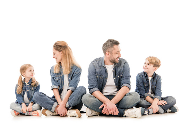 Szczęśliwa rodzina w dżinsy siedzi z skrzyżowanymi nogami na białym tle - Zdjęcie, obraz
